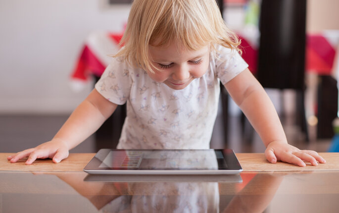 Jente med nettbrett Bildet viser en smilende, liten jente som står og kikker ned på er nettbrett som ligger på bordet