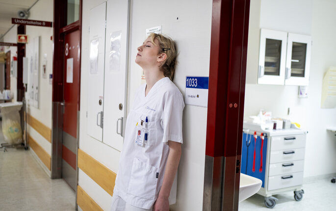 Bildet viser en sliten sykepleier som er lent mot veggen med ryggen.