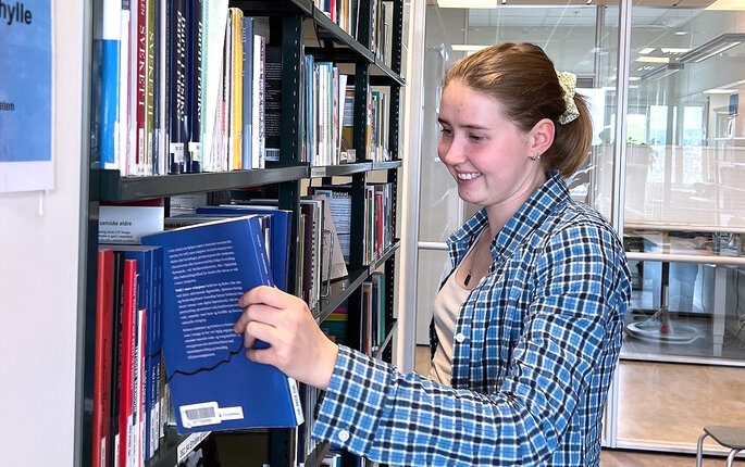 Bildet viser innleggsforfatteren som tar en bok ut av en bokhylle