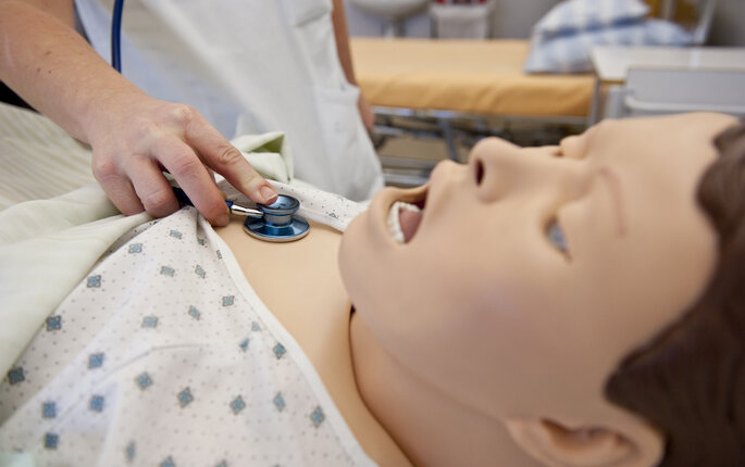 Bildet viser en hånd som holder et stetoskop på brystet til en simuleringsdukke