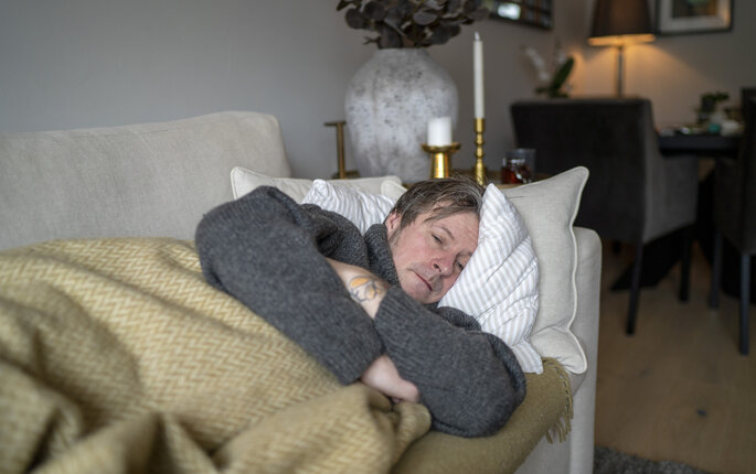 Bildet viser en mann som ligger på sofaen og er syk.