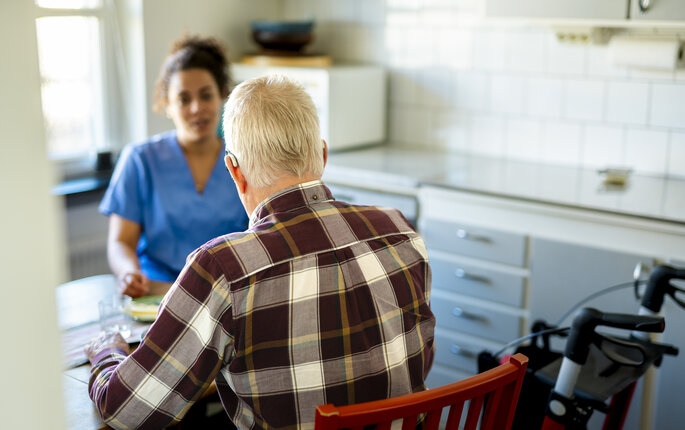 Bildet viser en mann som sitter med ryggen til kamera, vendt mot en pleier.