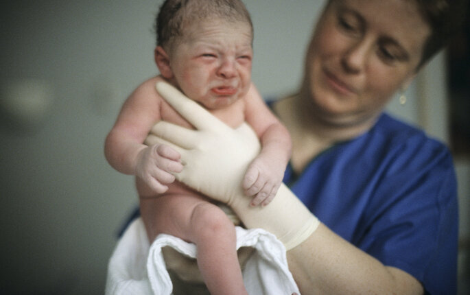 Bildet viser en jordmor som holder opp en nyfødt baby