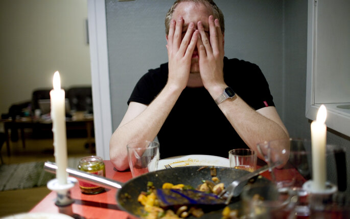 Bildet viser en mann som sitter ved et spisebord og holder seg til ansiktet.