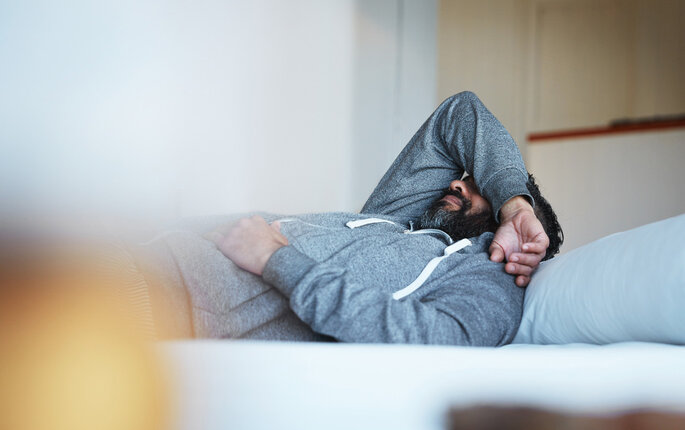 Bildet viser en ung mann som ligger på sofaen med høyre arm over hodet.
