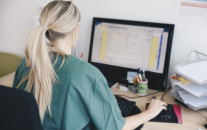 Bildet viser en sykepleier som sitter ved en datamaskin.