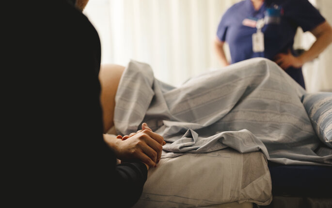 Bildet viser en kvinne som skal føde. I bakgrunnen: en jordmor.