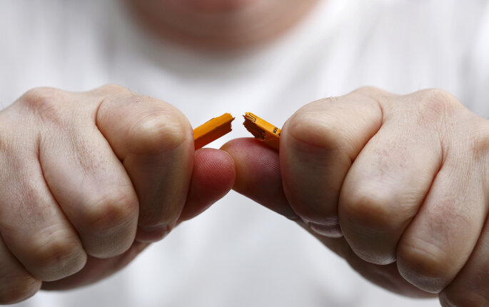 Nærbilde av at en mann knekker en blyant i to.