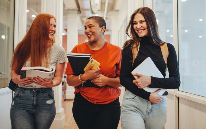 Bildet viser tre studenter som går i en gang på skolen og ler sammen