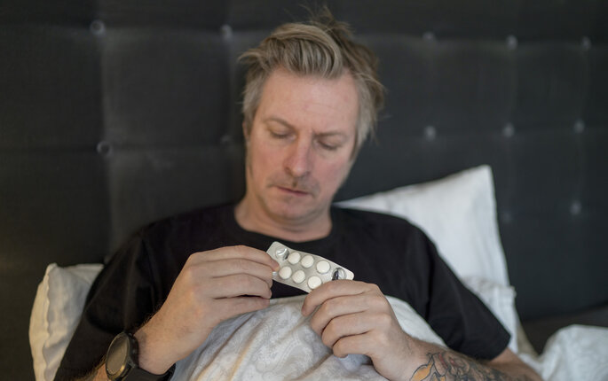 Bildet viser en mann i senga med tabletter.