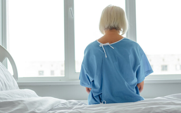 Bildet viser en pasient bakfra. Hun sitter på en sykehusseng og ser framfor seg.