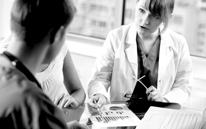 Bildet viser ei dame i hvit frakk som viser to personer et ark med et diagram på.