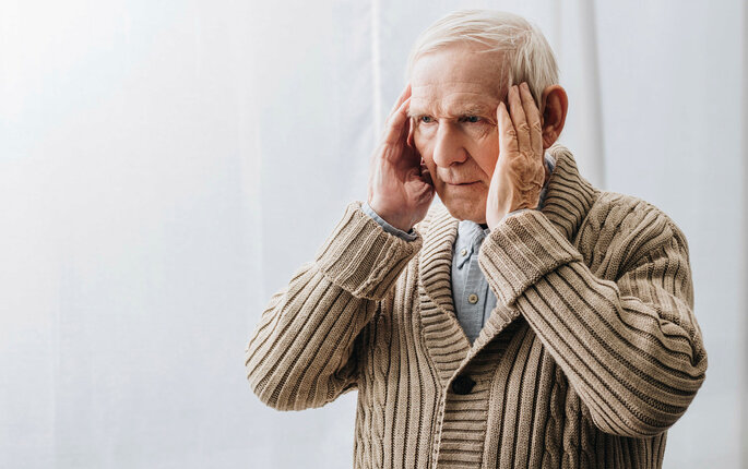 Bildet viser en eldre mann som holder hendene mot tinningene.