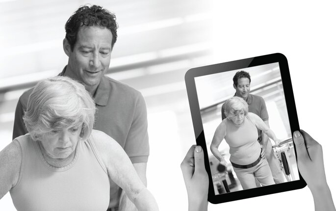 Bildet viser hjemmehjelp som trener med ei eldre dame til instrukser fra fagperson mottatt via ipad.