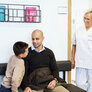 Bildet viser en sykepleier som henvender seg til en liten gutt og hans far på venteværelset