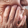 Bildet viser en eldre kvinne som tar seg til ansiktet ved munnen