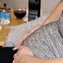 Bildet viser magen til en gravid dame som sitter i en stol. I hånda holder hun en sigarett. På bordet bak står et askebeger fullt av sneiper og et glass med rødvin