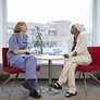 Bildet viser to sykepleiere som sitter og prater sammen ved et vindu