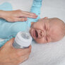 Bildet viser et spedbarn som storgråter. En hånd ligger trøstende på magen til barnet, mens den andre hånden holder en tåteflaske og skal til å gi barnet