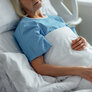 Bildet viser en eldre kvinne i en sykehusseng