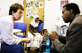 Bildet viser helsepersonell i samtale med tolk fra Somalia på Ullevål, migrasjonshelse Oslo. To somaliske barn leker i bakgrunnen. 
