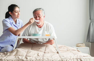 Bildet viser en japansk sykepleier som mater en eldre mann.