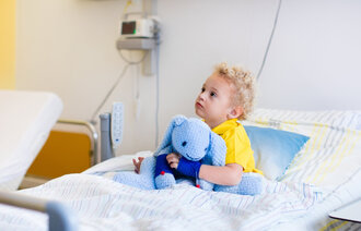 Bildet viser et lite barn som sitter i en sykehusseng.