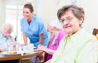 Fornøyde eldre på sykehjem med ansatt i bakgrunnen