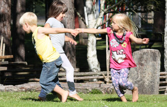 Tre nordisk utseende barn leker i ring. Lettkledde i sommervær. 