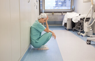 Sliten kvinnelig lege  med hette over håret hviler mot veggen i sykehuskorridor 