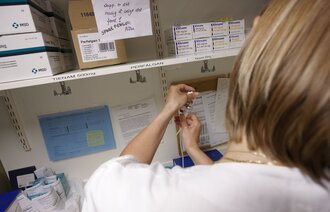 Bildet viser en sykepleier på et medisinrom som trekker opp en sprøyte.