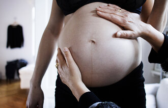 Bildet viser en gravid mage som blir undersøkt av to hender.