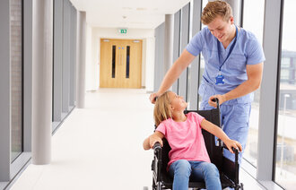 En mannlig sykepleier sammen med et barn i rullestol