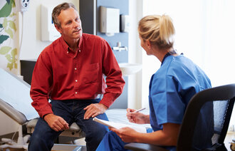 Bildet viser en mannlig pasient som er i konsultasjon med en kvinnelig sykepleier. Han sitter på en sykehusseng, og hun har et skjema i hånda.