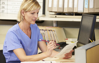 Bildet viser en sykepleier som sitter ved en pult og gjør papirarbeid