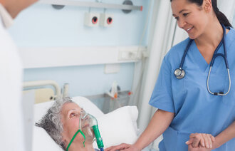 Bildet viser en pasient i sengen med maske, mens en sykepleier står ved siden av