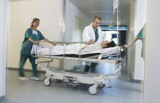 Bildet viser en pasient i en sykehusseng som blir trillet av helsepersonell