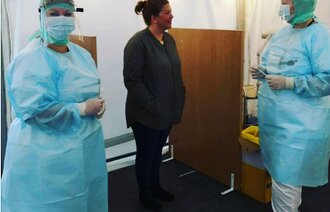 Bildet viser to sykepleiere i smittevernsutstyr og en uten.