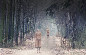 Bildet viser en eldre kvinne som går alene på en sti i skogen.