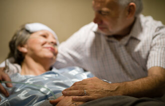 Bildet viser eldre mann ved sykeseng til kona