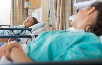 Bildet viser to kvinnelige pasienter som ligger i hver sin seng i operasjonsklær og ser på hverandre