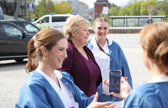 Bildet viser Ida Gerø med mobiltelefon, i bakgrunnen statsminister Erna Solberg og andre sykepleiere.