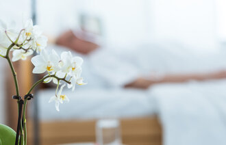 Bildet viser en orkidé i forgrunnen og en mann liggende i sengen i bakgrunnen