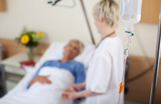Bildet viser en sykepleier som står ved siden av en sengeliggende pasient