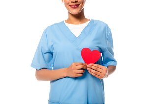 Bildet viser en sykepleier som holder et papirhjerte foran hjertet sitt