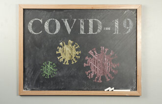 Bildet viser en skoletavle. På tavlen står det skrevet covid-19 og det er tegninger av koronaviruset.