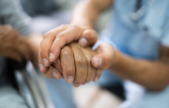 Bildet viser en sykepleier som holder en eldre pasient i hånden.