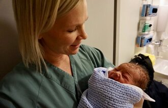 Bildet viser jordmoren Helene Normann Furnes med et nyfødt barn i armene.