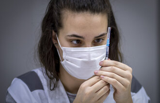 Bildet viser en sykepleier som sjekker en ferdig fylt vaksine fra Pfizer/Biontech.