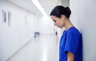 Bildet viser en sykepleier som står inntil en vegg. Hun er sliten